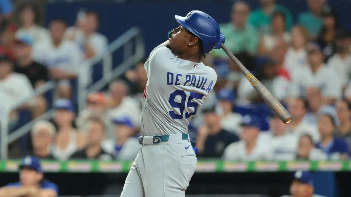 Baseball player in white uniform and blue helmet swings a bat during play.
