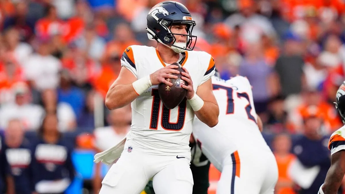 Denver Broncos quarterback wearing number 10 holds the football as teammates block nearby.