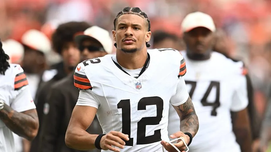 Football player wearing a white number 12 jersey stands on the field with teammates behind him.