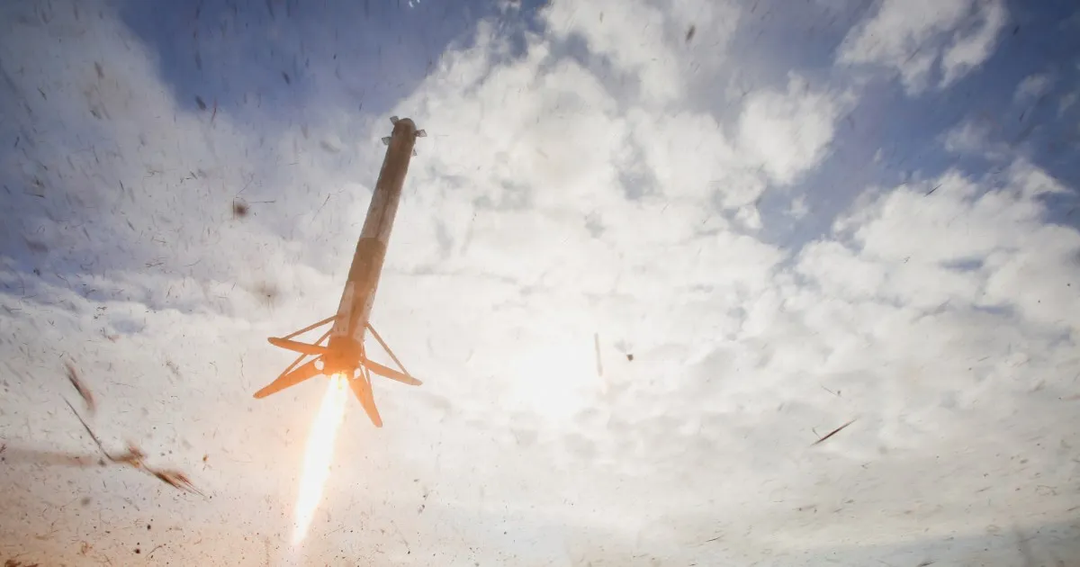Rocket ascending against a partly cloudy sky, viewed through a marked or dirty window.
