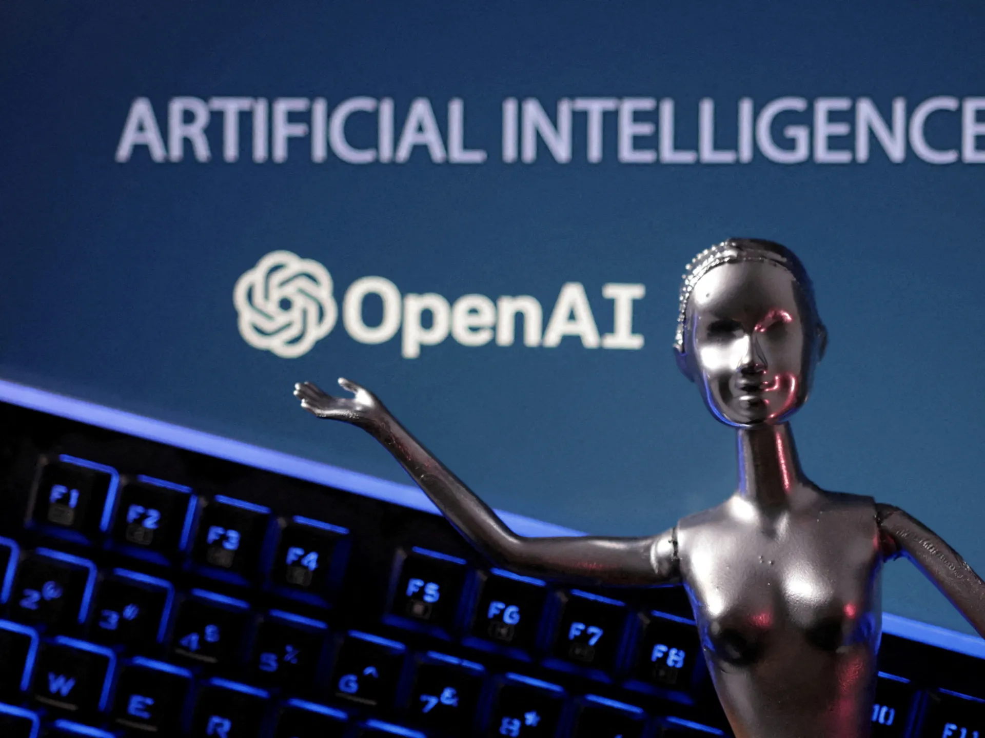 Metallic humanoid robot stands before an OpenAI logo and artificial intelligence text above a glowing keyboard.