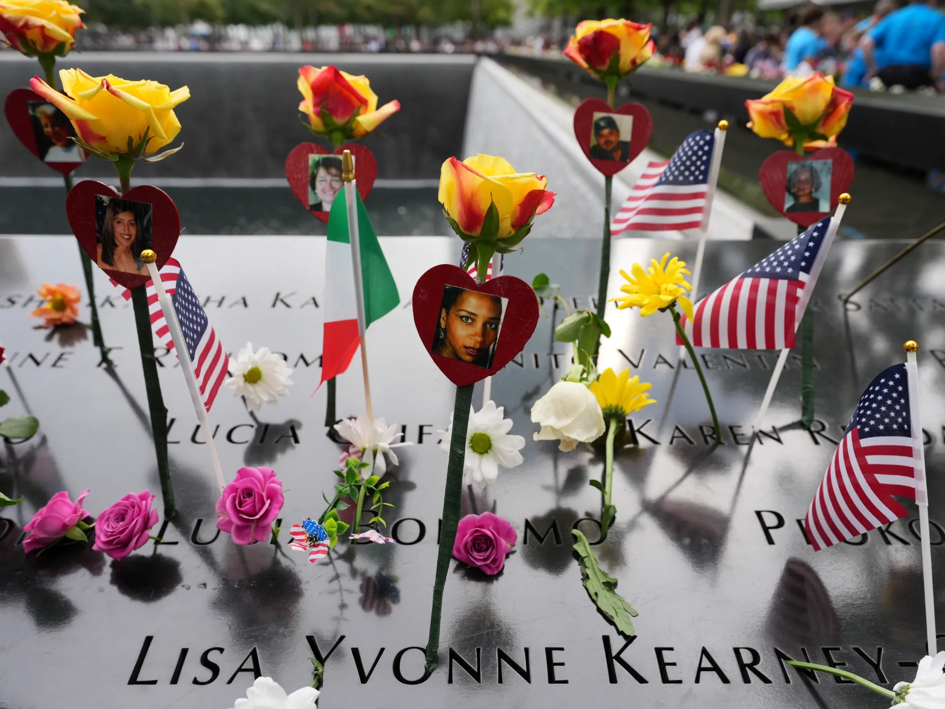 Flowers, memorial photographs, and American flags arranged on a polished memorial reflecting pool