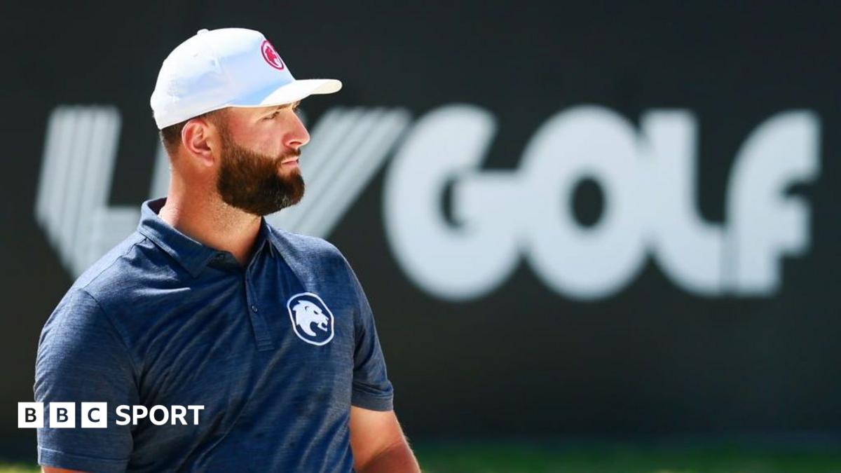 Bearded golfer in a white cap and navy polo stands before a LIV Golf logo.
