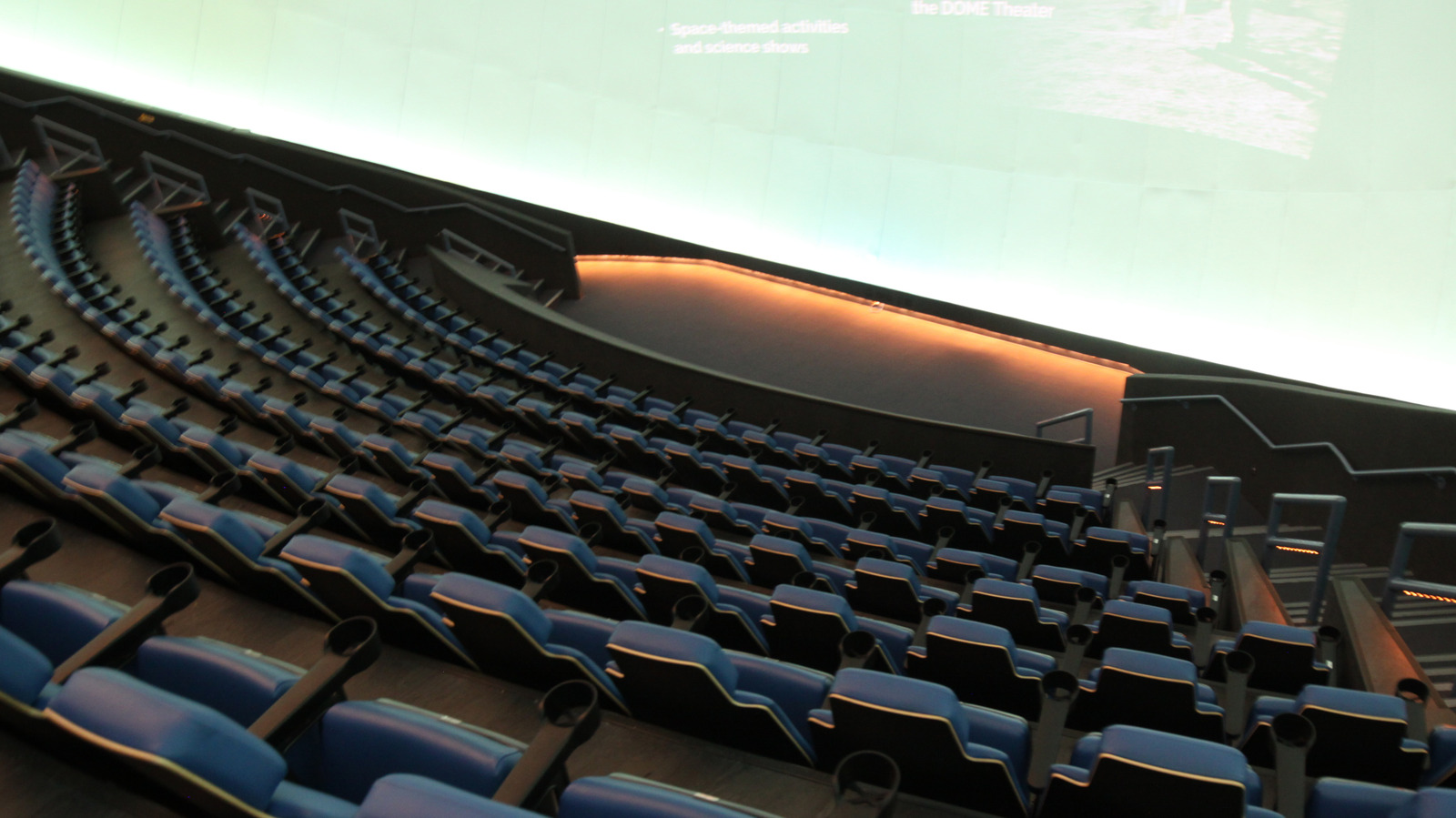 Empty large-format theater with curved rows of blue seats facing a bright domed screen