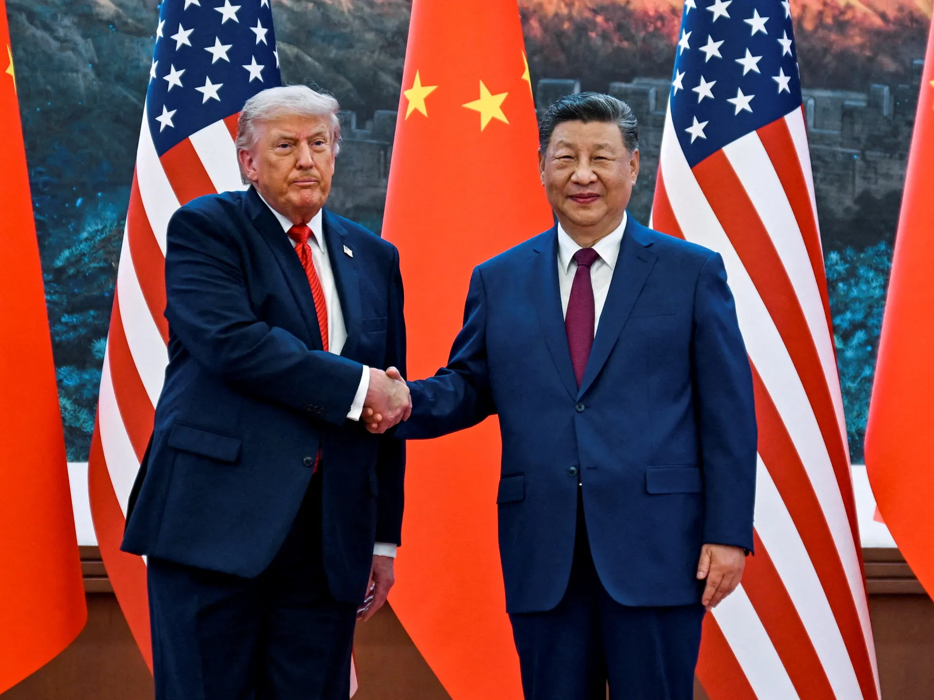Two suited leaders shake hands before alternating US and Chinese flags.