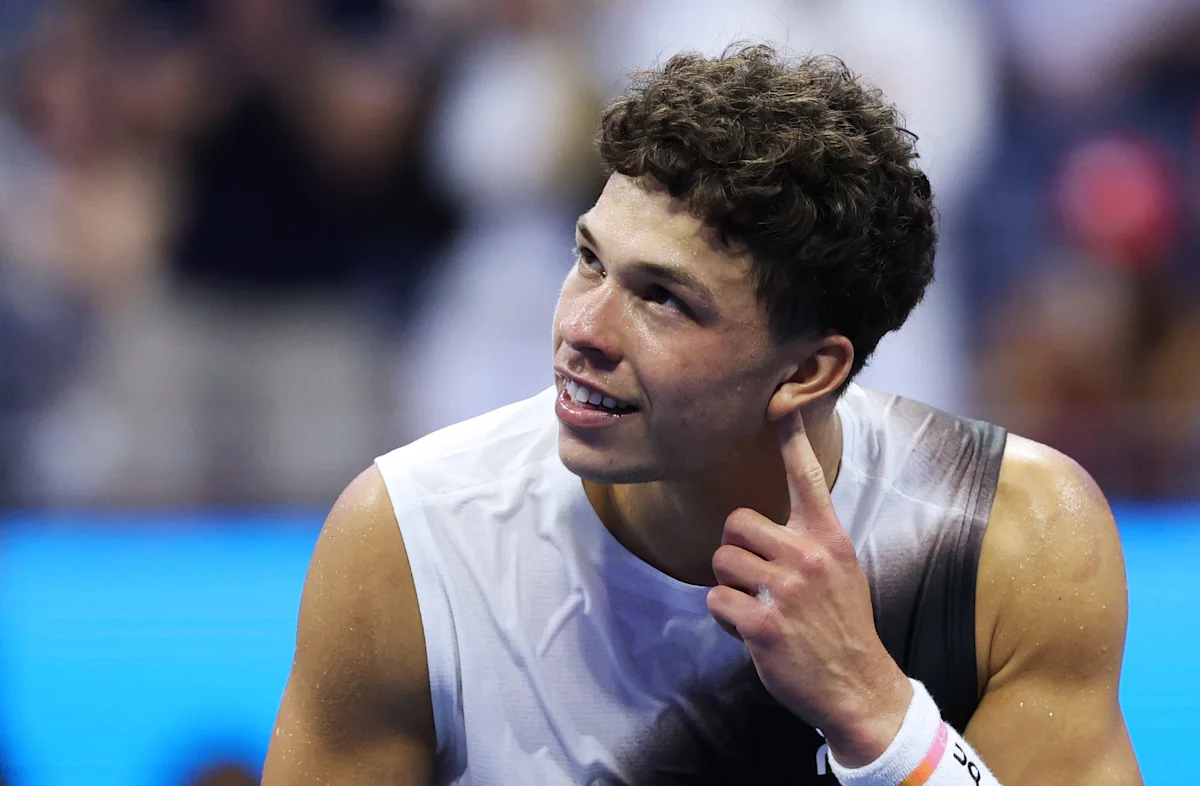 Tennis player in white sleeveless shirt touching his neck during a match