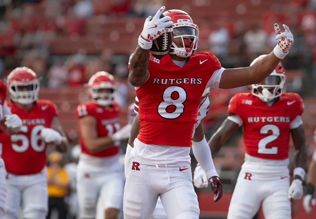 Rutgers football player in red No. 8 jersey celebrates while holding a football during a game.