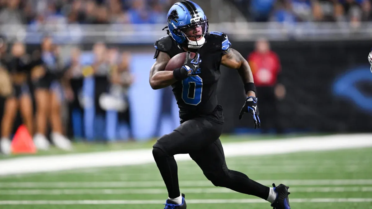 Football player in black and blue uniform runs with the ball on a field.