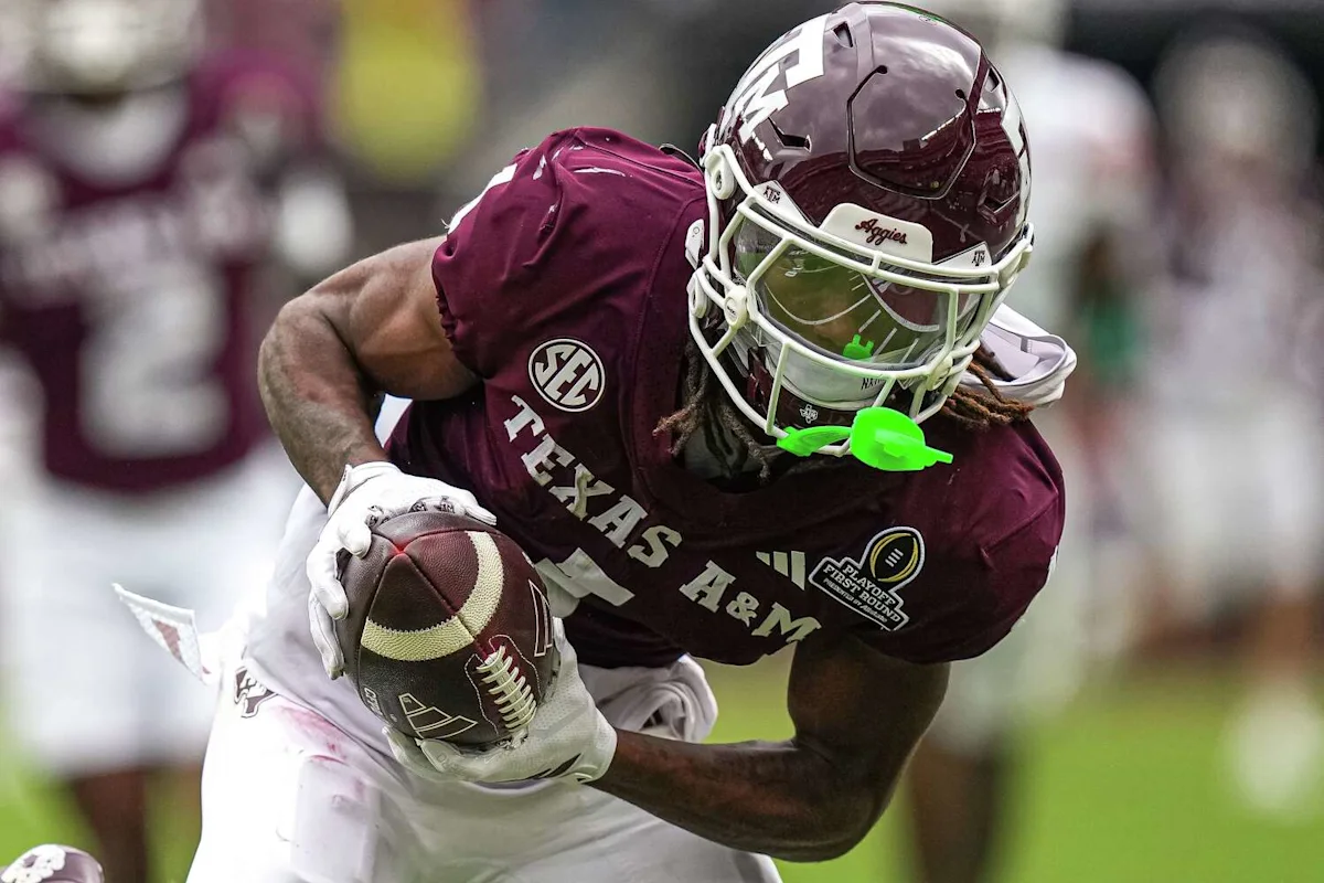 Texas A&M football player in maroon uniform and helmet runs with the ball.