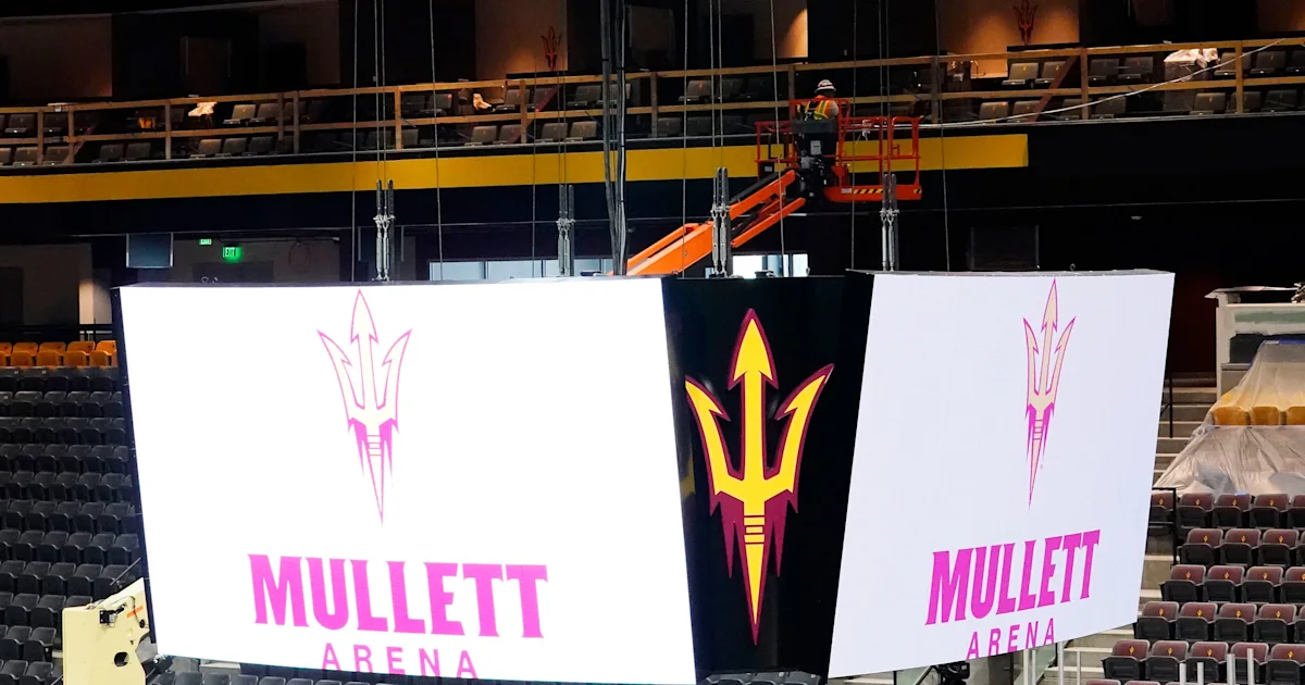 Arena scoreboard panels display pink Mullett Arena lettering and a yellow pitchfork emblem as a worker operates a lift.