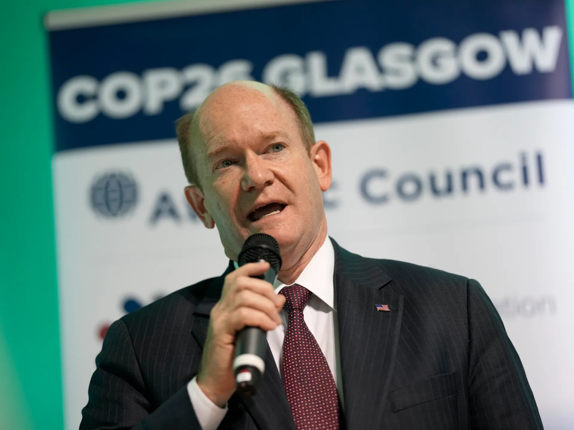 Man in suit speaking into a microphone before a conference backdrop