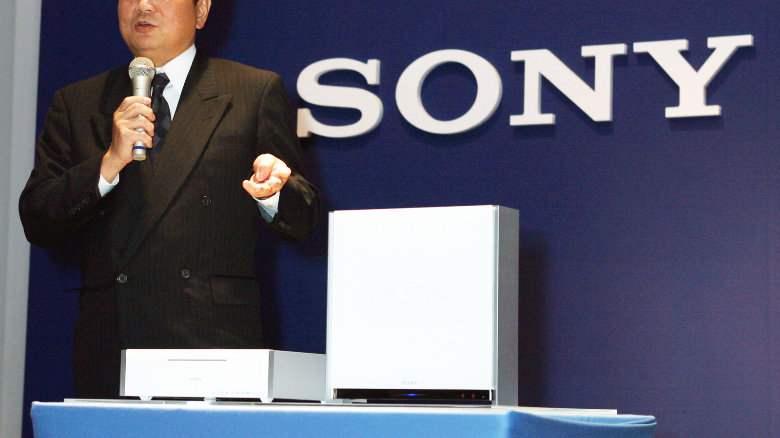 Man in suit holding a microphone beside white Sony electronics on a stage