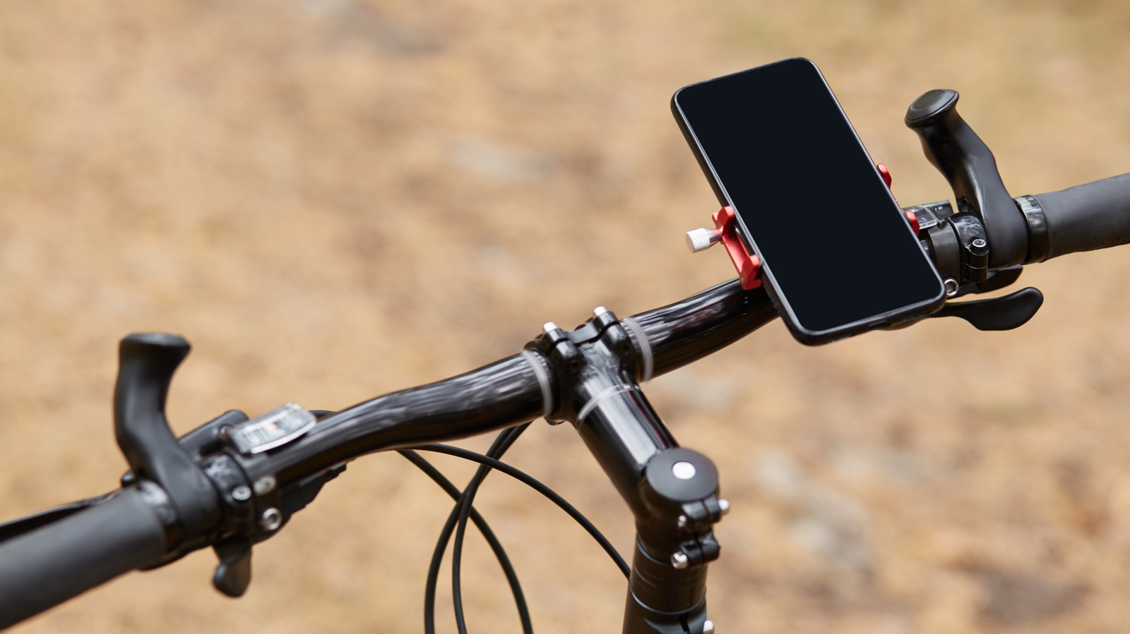 A smartphone with a blank screen mounted on bicycle handlebars against a blurred tan background.