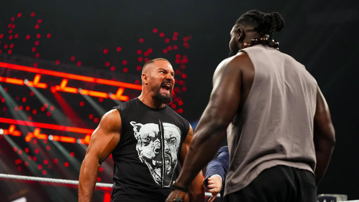 Two wrestlers face off inside a ring beneath red arena lights.