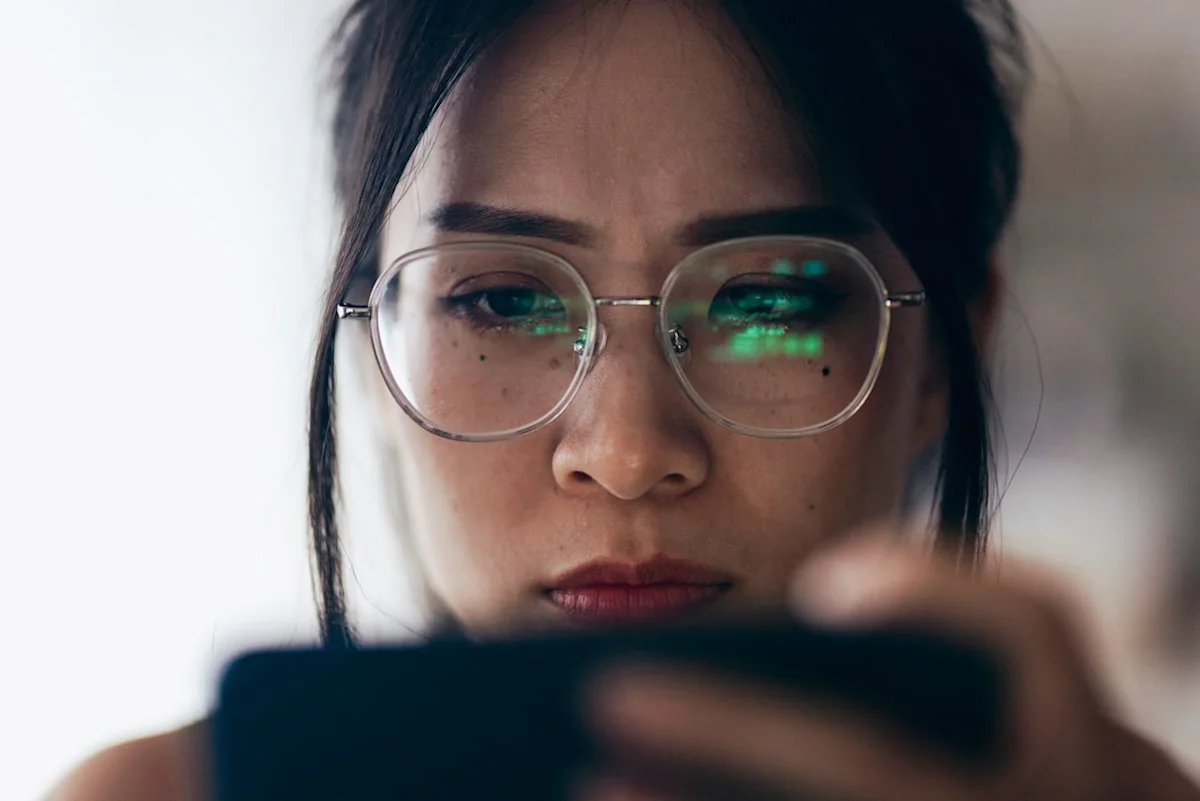 Close-up of a woman wearing glasses and looking at a smartphone with green screen reflections