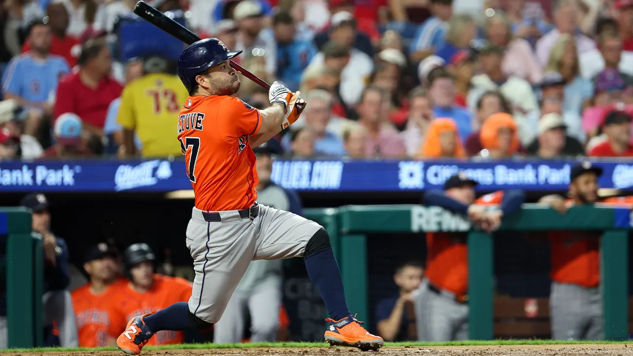 Baseball player in orange jersey swings at a pitch during a game.