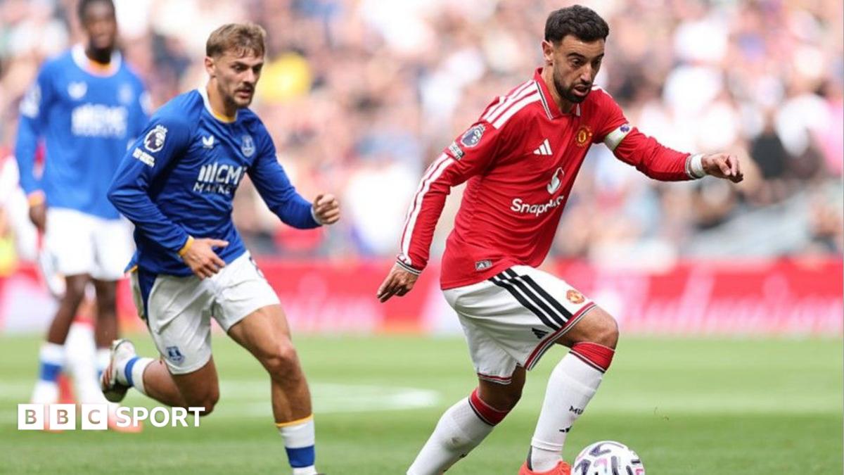 Footballers in red and blue kits chase the ball during a match.
