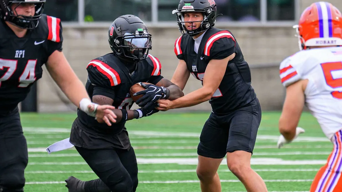 RPI players in black uniforms execute a handoff as a Hobart player approaches on the field.