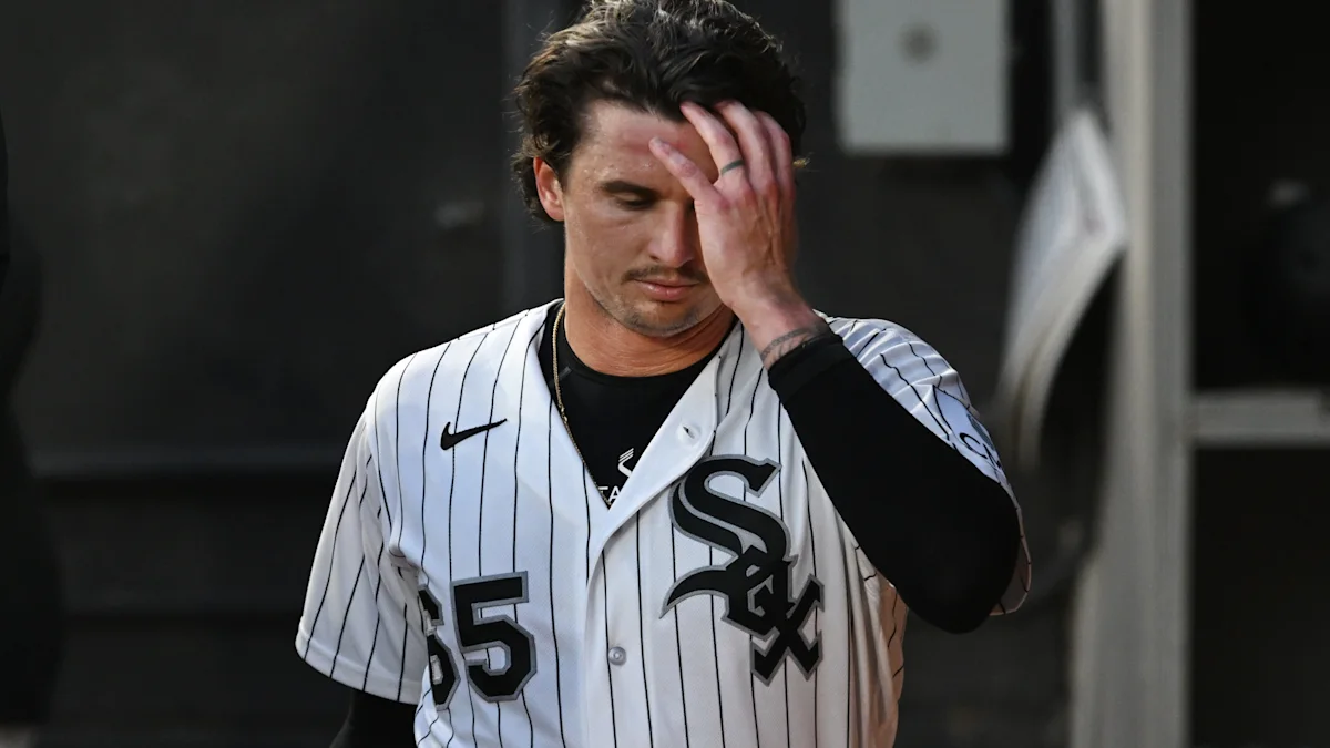 A White Sox player in a pinstriped uniform touches his forehead while walking off the field.