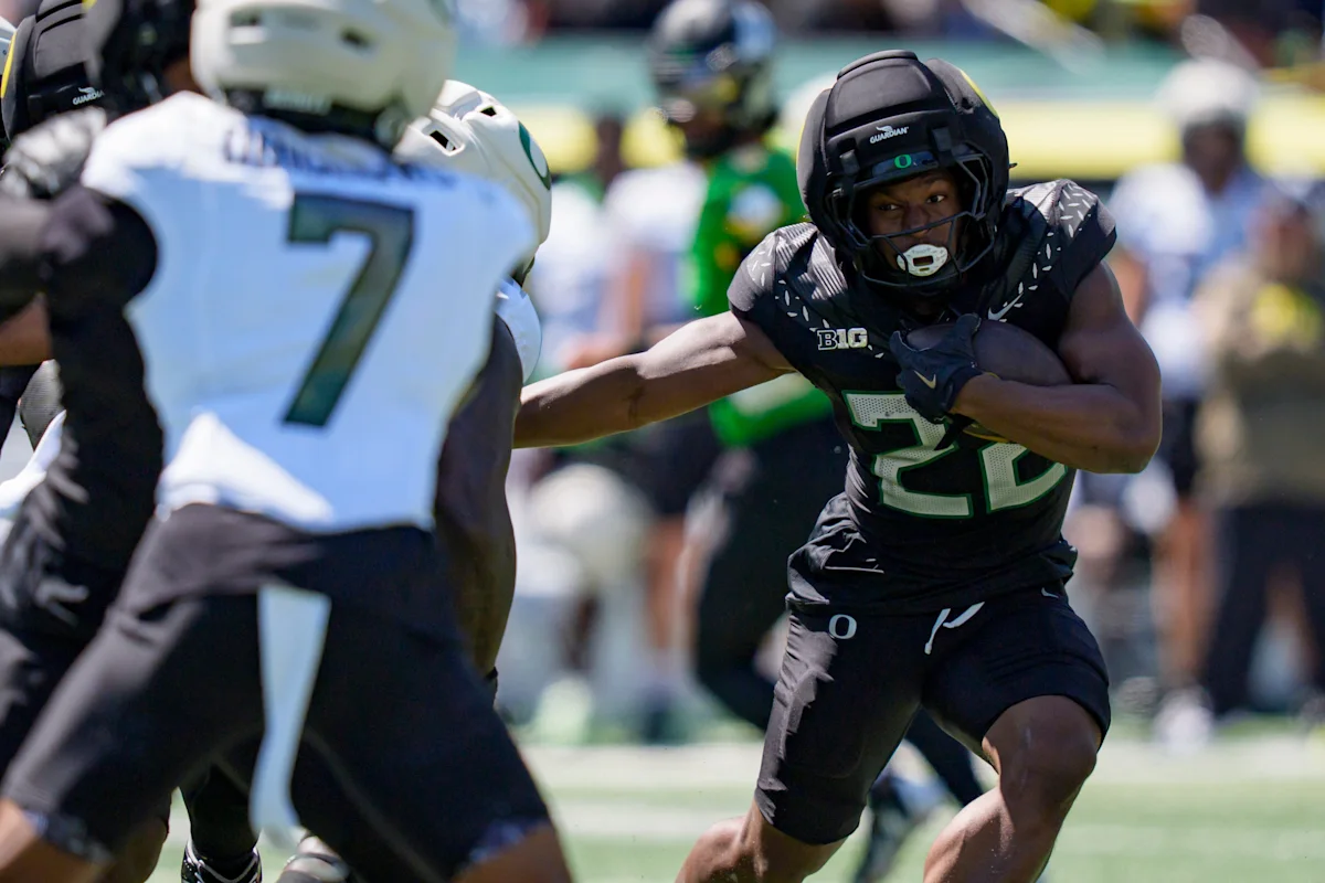 Oregon football player in black uniform runs with the ball past a defender.