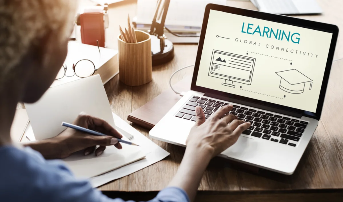 Person writing notes beside a laptop displaying a global connectivity and learning graphic