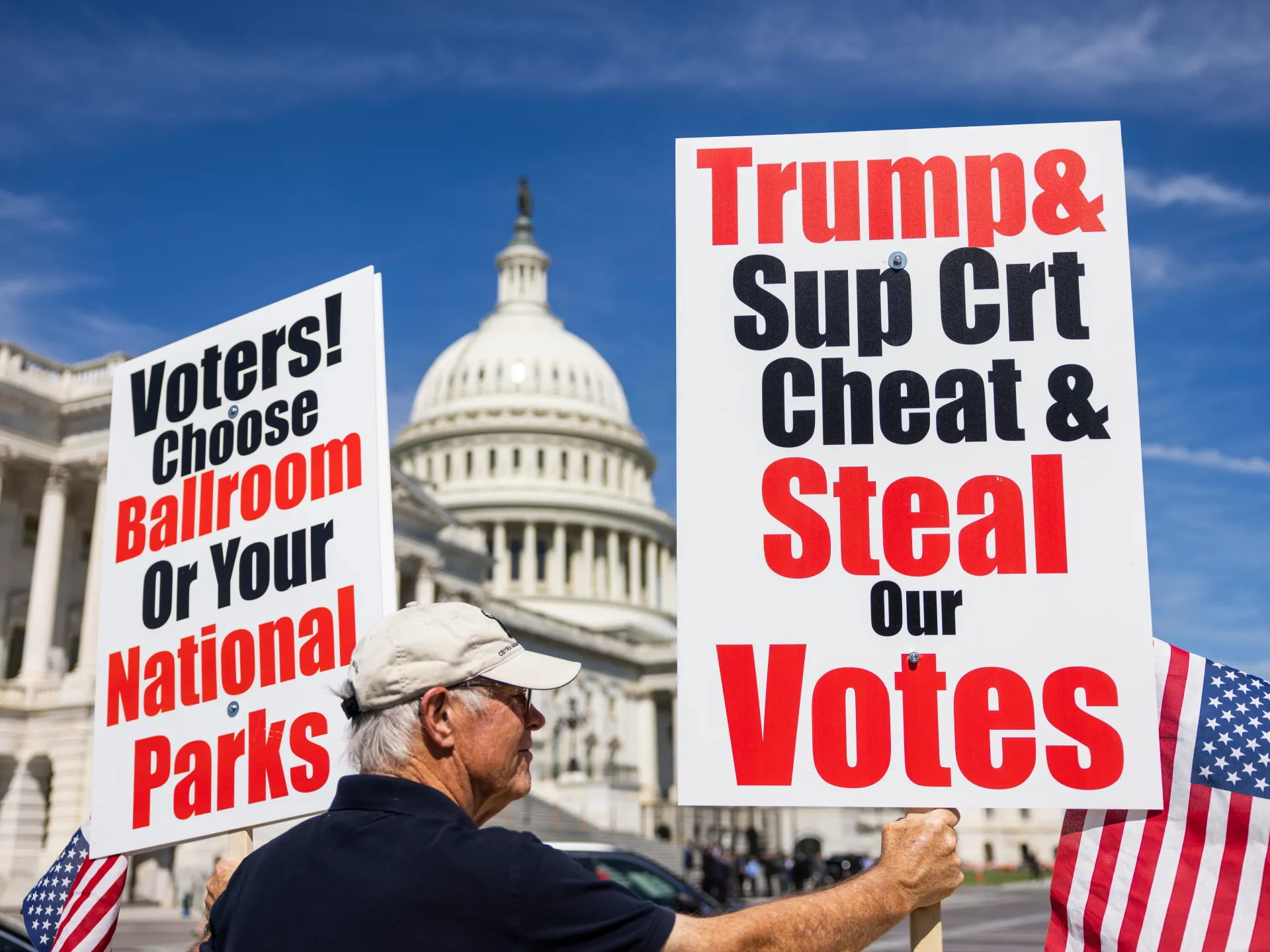 People hold political signs outside the US Capitol beneath a blue sky.