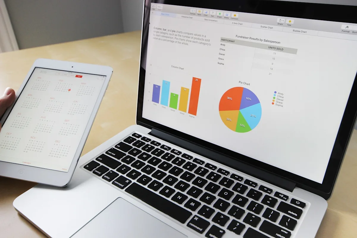 Laptop displaying sales charts beside a tablet showing a calendar on a desk