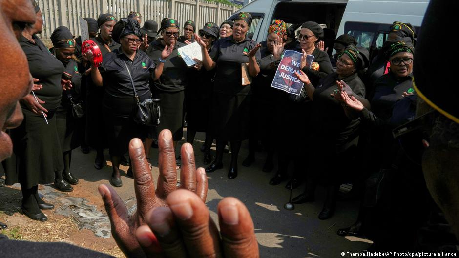 Women in black clothing gather outside a vehicle, holding signs and raising hands.