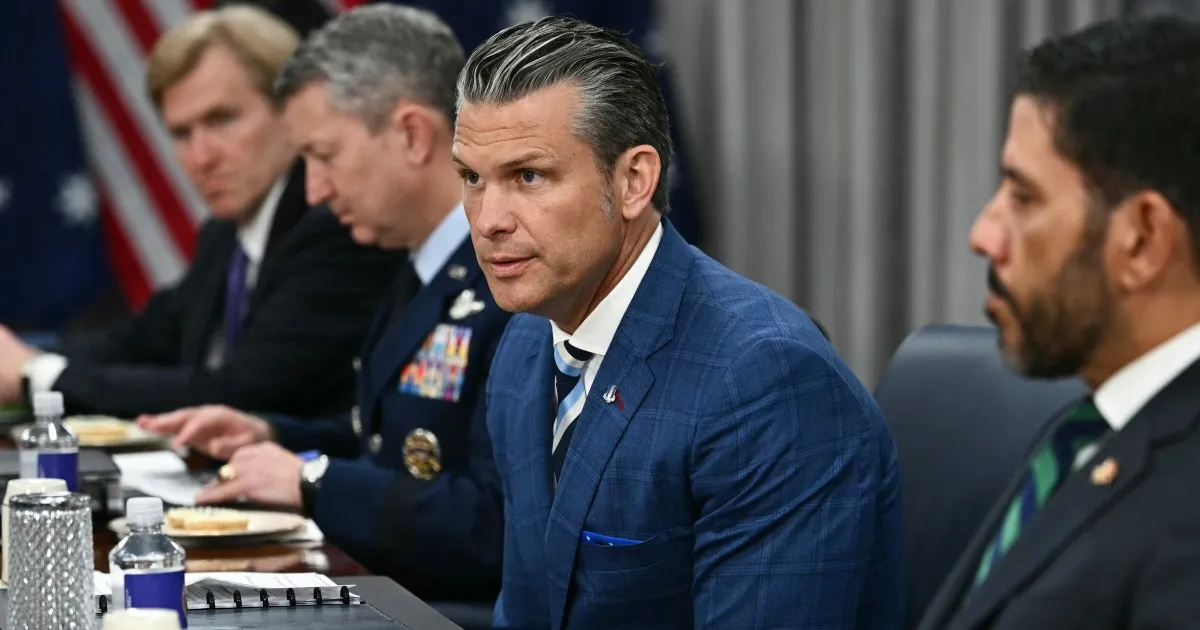 Officials sit at a conference table, with a suited man in blue prominent in foreground.