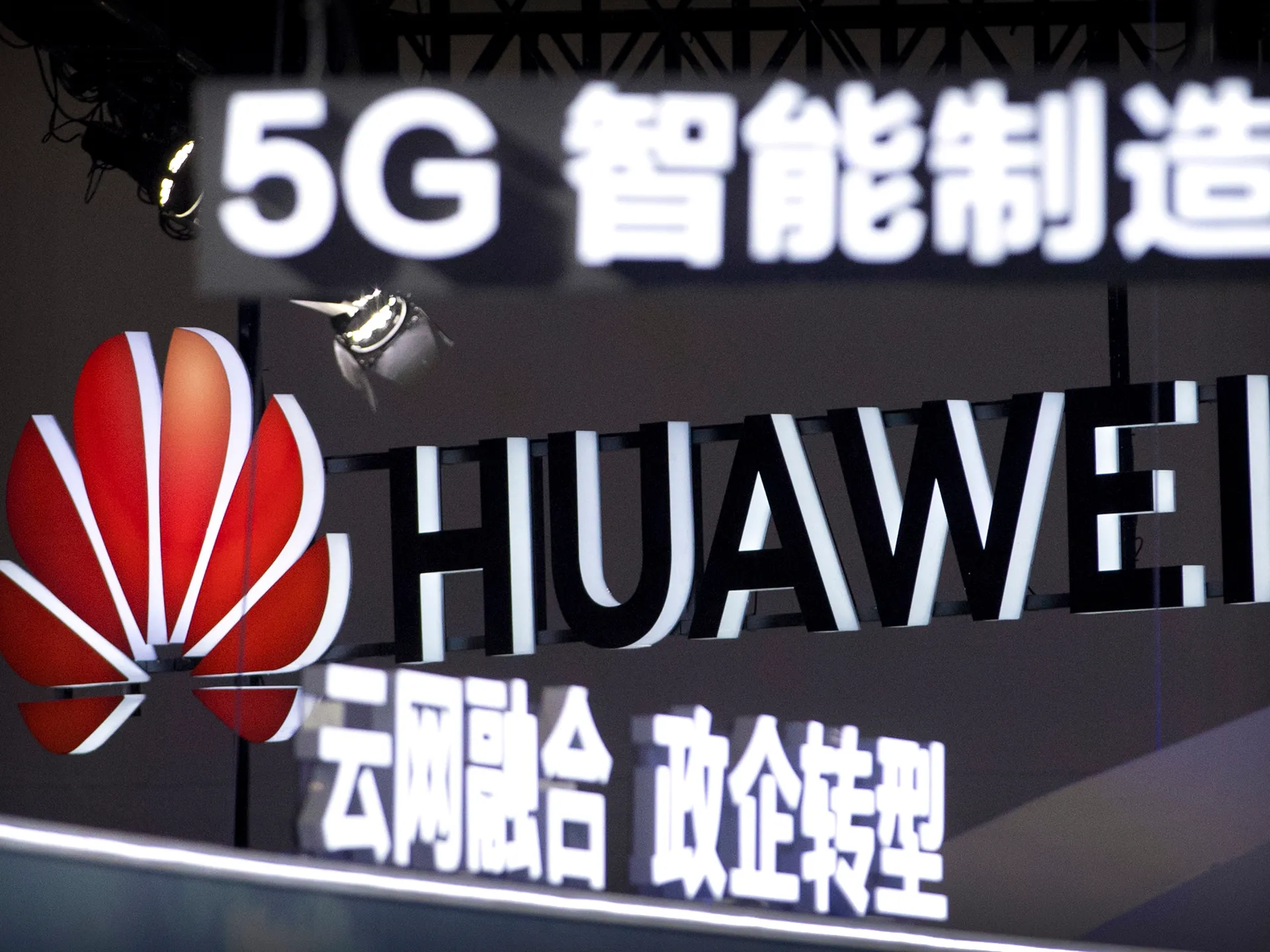 Illuminated Huawei logo and 5G signage displayed above Chinese characters at an indoor exhibition.