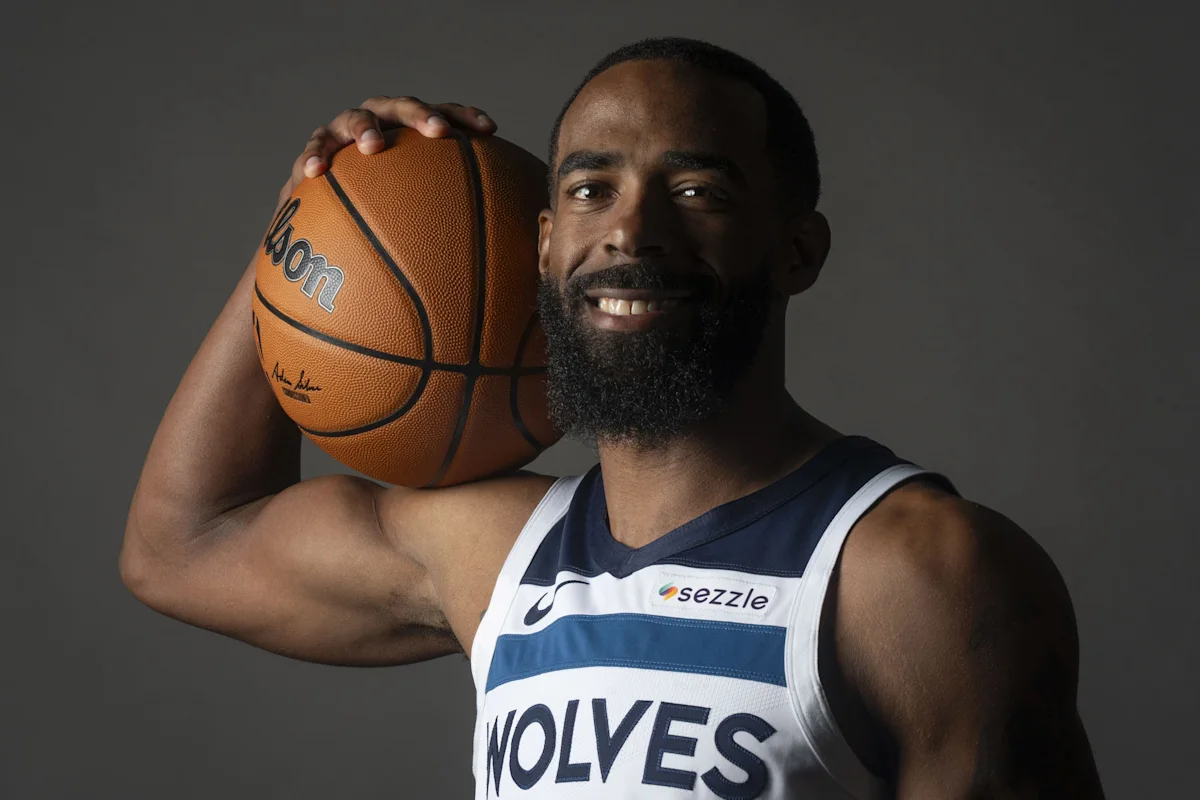 Basketball player holding a basketball against his shoulder while wearing a Wolves jersey
