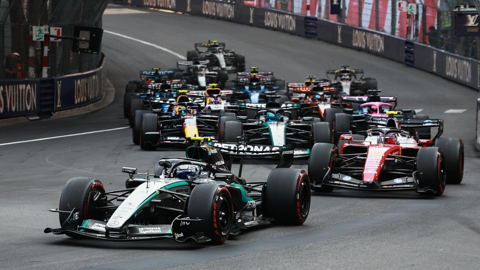 A tightly packed field of Formula 1 cars navigates a narrow street circuit.