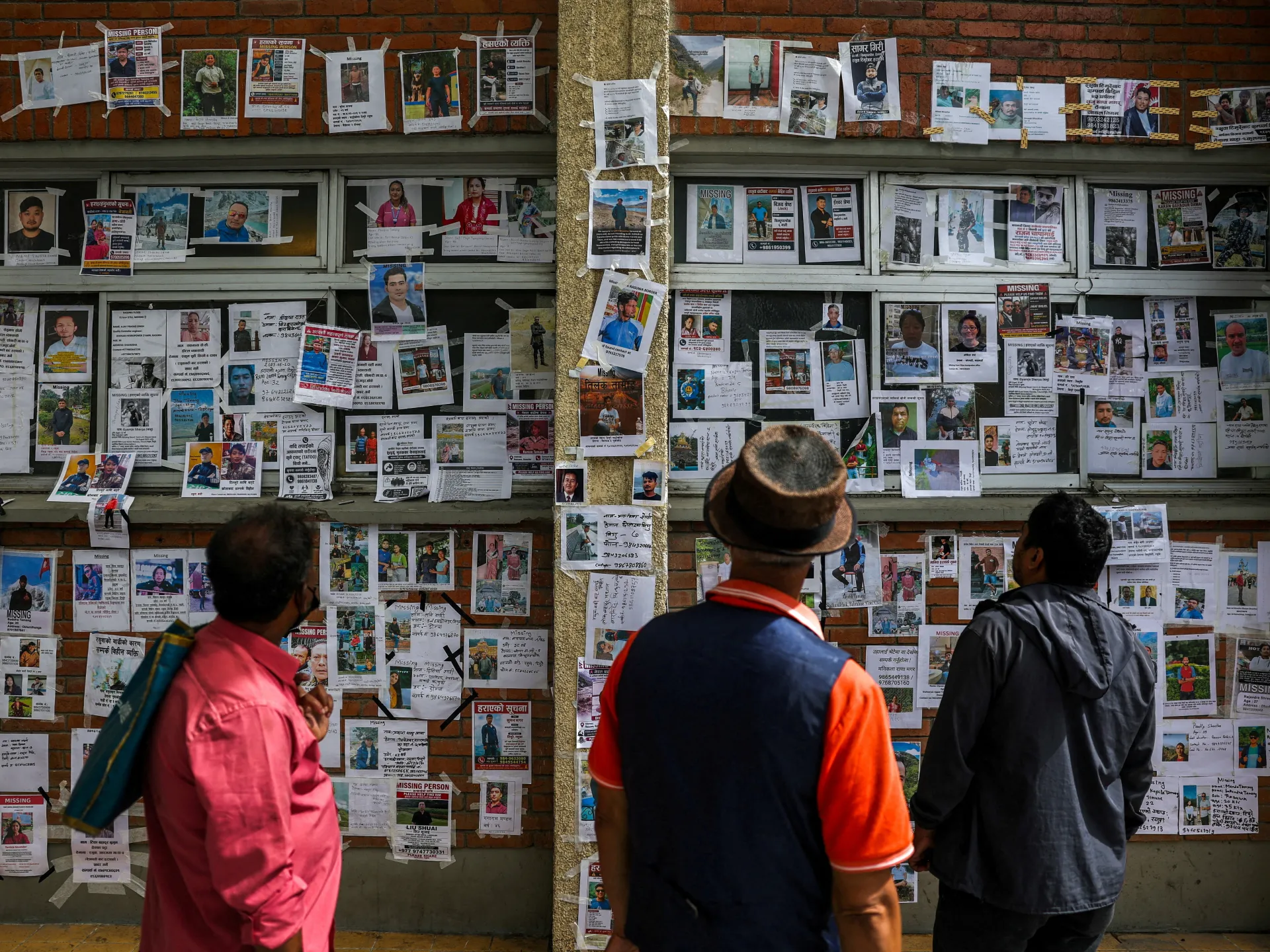 People examine a wall densely covered with missing-person posters and photographs.