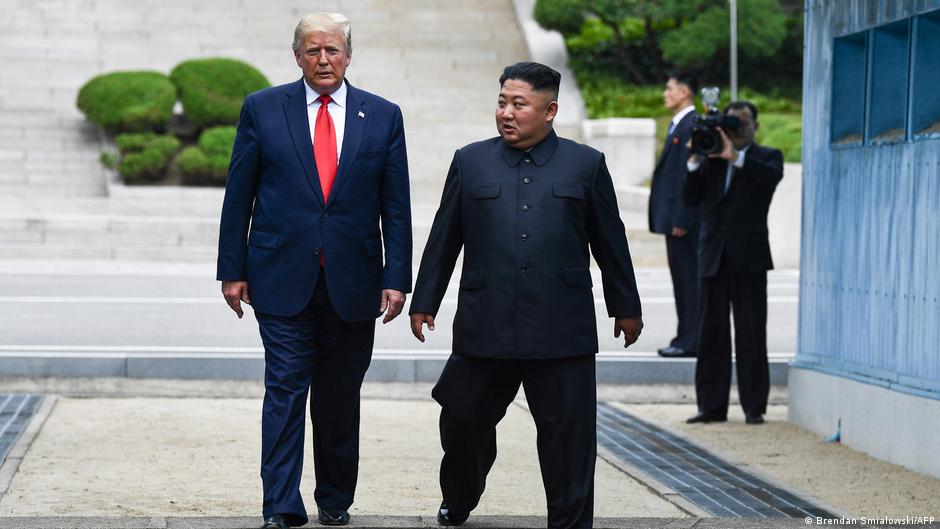 Two men walk beside a blue building, with photographers visible behind them.