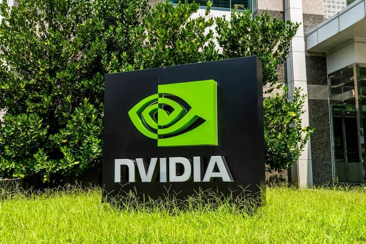 Nvidia logo sign displayed outside a modern building, surrounded by leafy trees and grass.