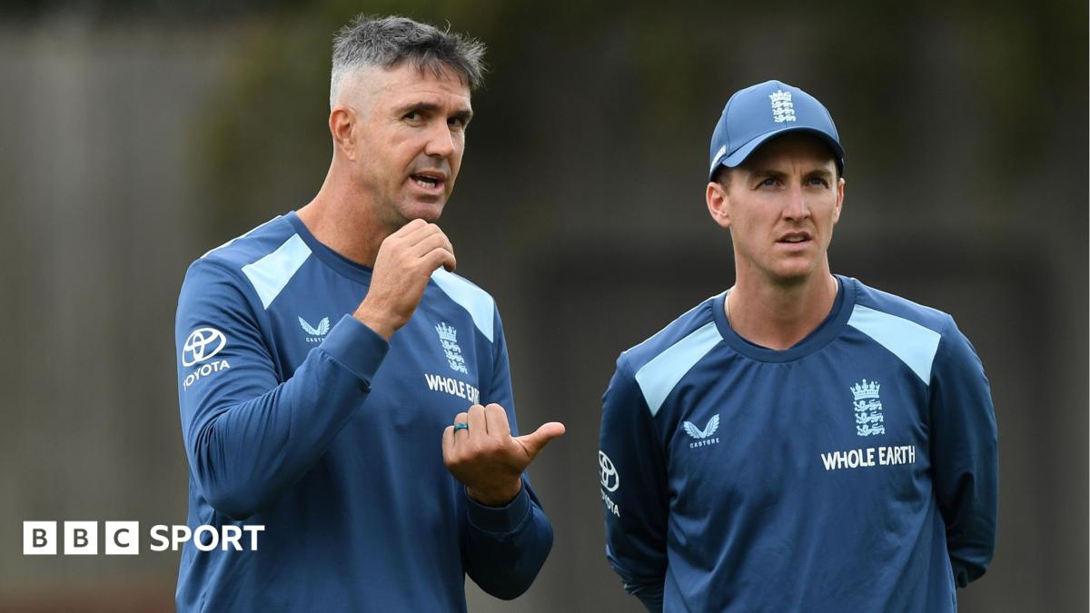 Two England cricket figures in blue training tops talk during a practice session.