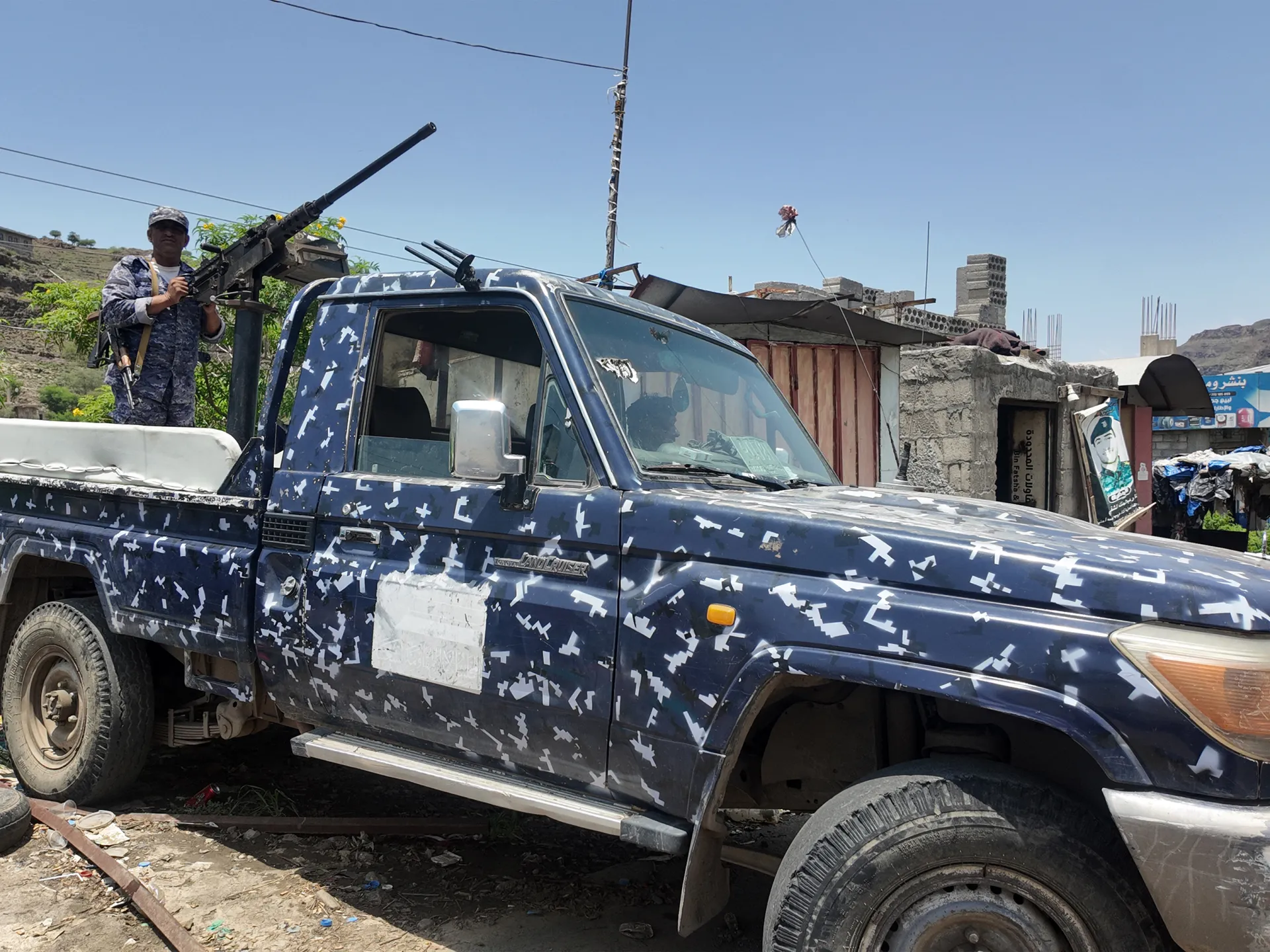 Camouflaged pickup truck mounted with a heavy machine gun, with a uniformed man standing beside it.