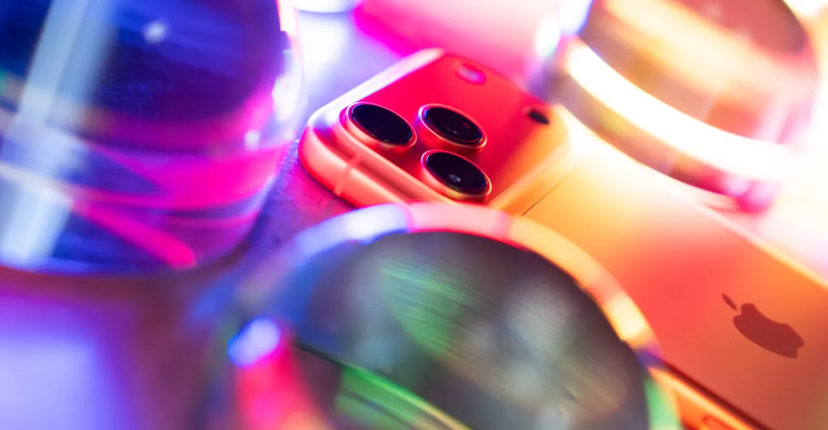 Close-up of an iPhone, smartwatch and colorful electronic devices under vivid neon lighting