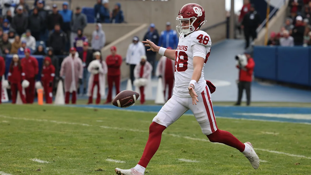 Oklahoma player in a white uniform punts a football during a game.