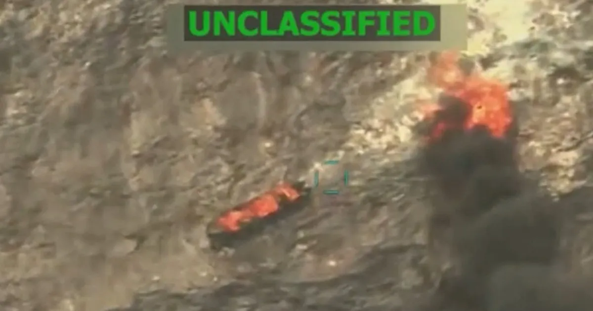Blurry aerial footage shows a burning object amid dark smoke, with an UNCLASSIFIED label overhead.