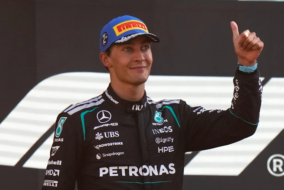 Formula One driver in Mercedes racing suit and Pirelli cap gives a thumbs-up gesture
