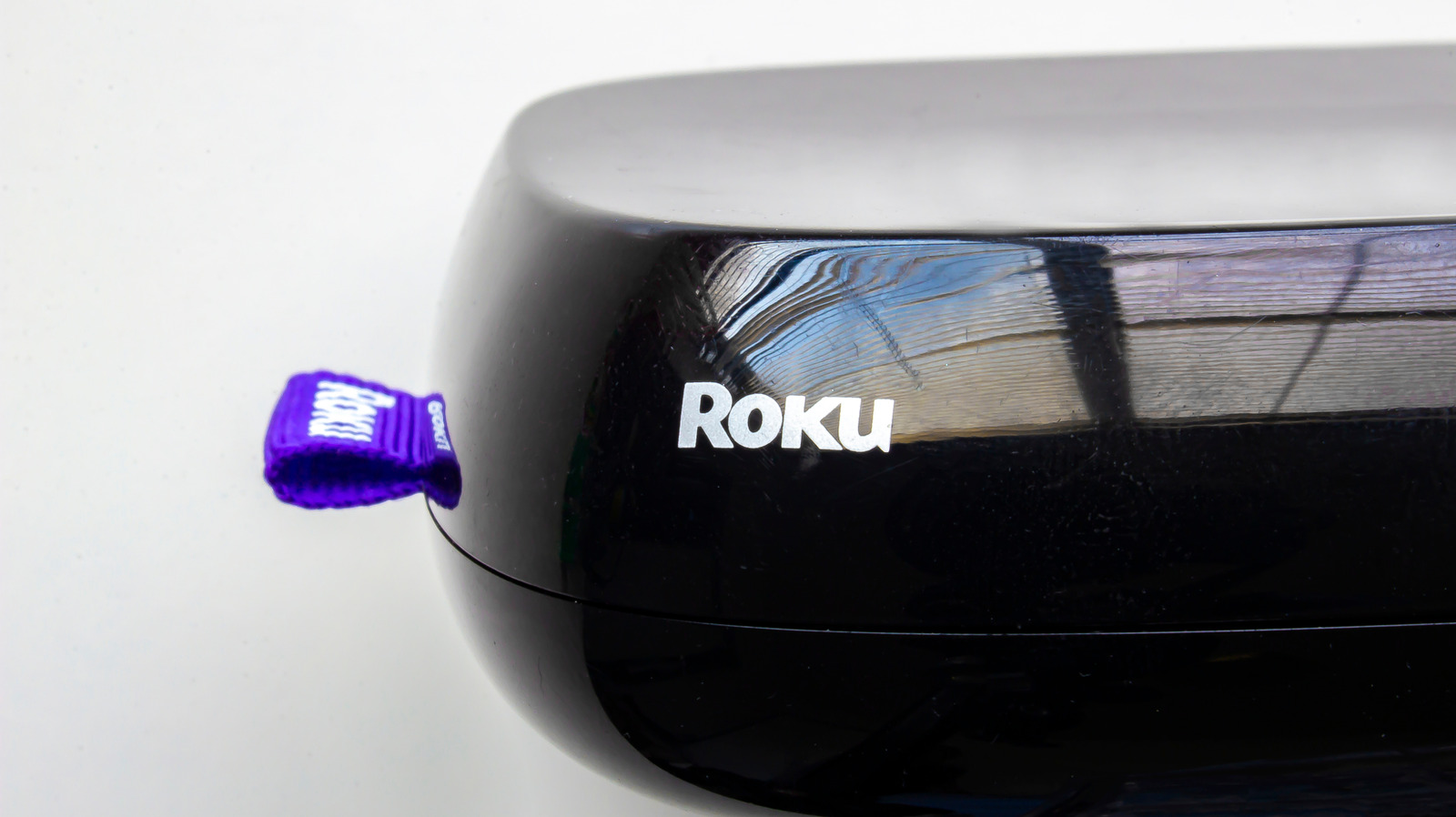 Close-up of a black Roku device with a purple strap attached beside its logo.