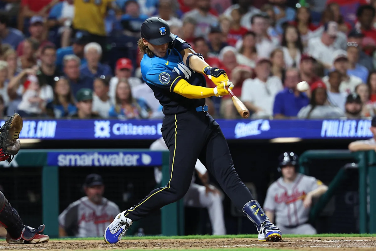 A baseball player in blue and yellow swings at a pitch during a game.