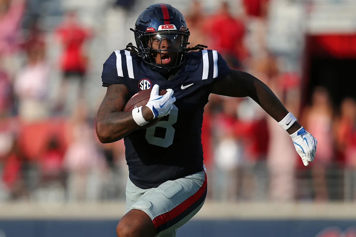 LSU football player in navy uniform runs with the ball during a game
