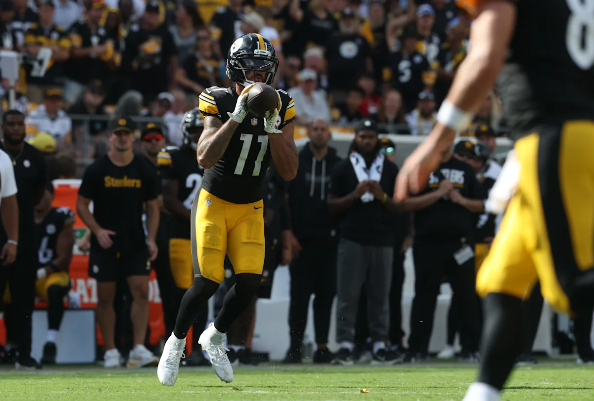 Pittsburgh Steelers receiver in uniform catches a football during a game as teammates and fans watch.
