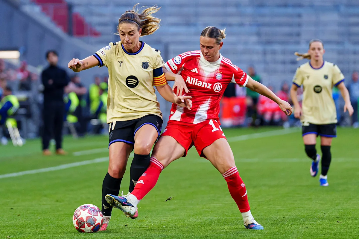 Two women’s soccer players in Barcelona and Bayern Munich kits compete for the ball on a field.