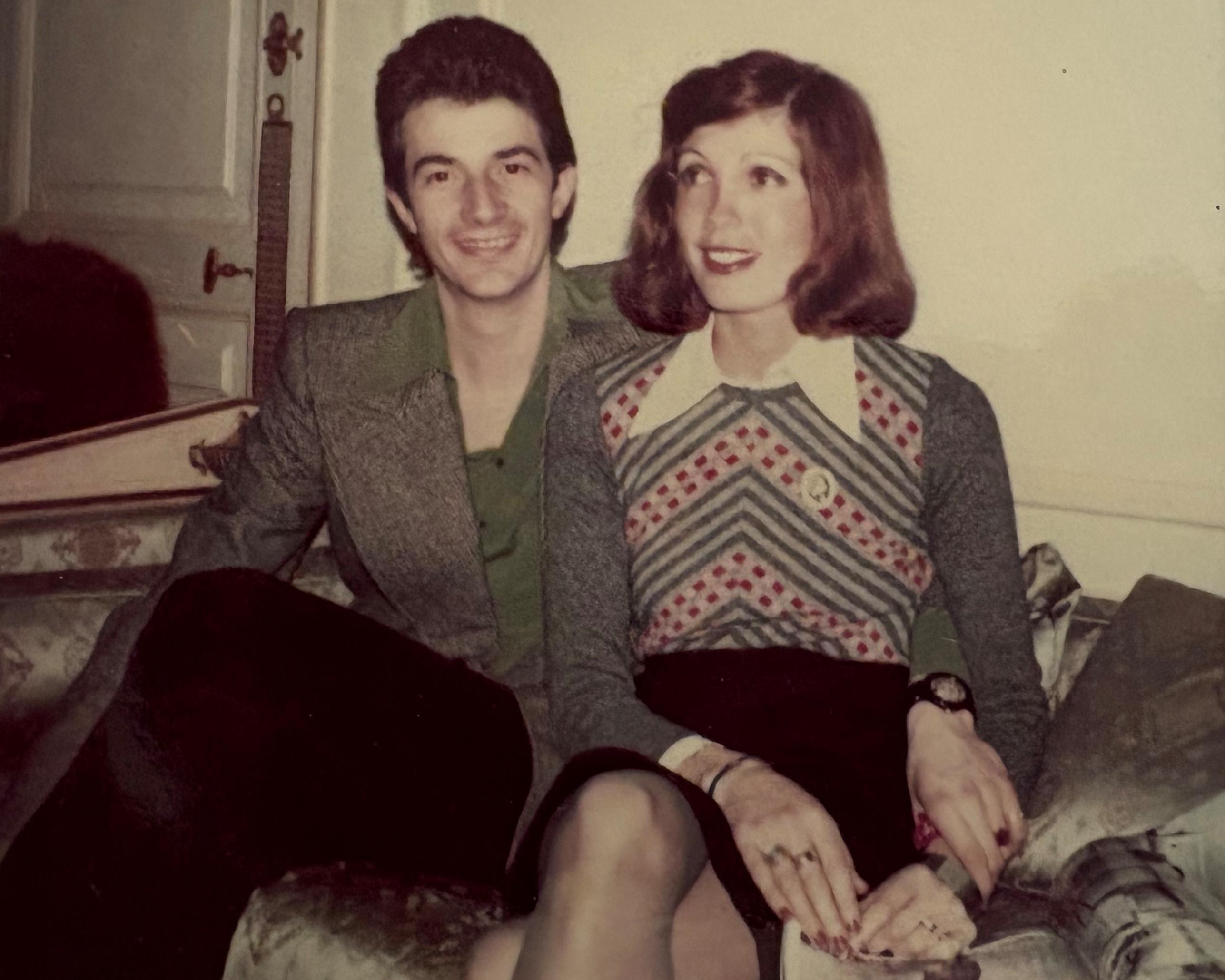 Young couple seated together indoors, wearing vintage clothing, with a small dog beside them.