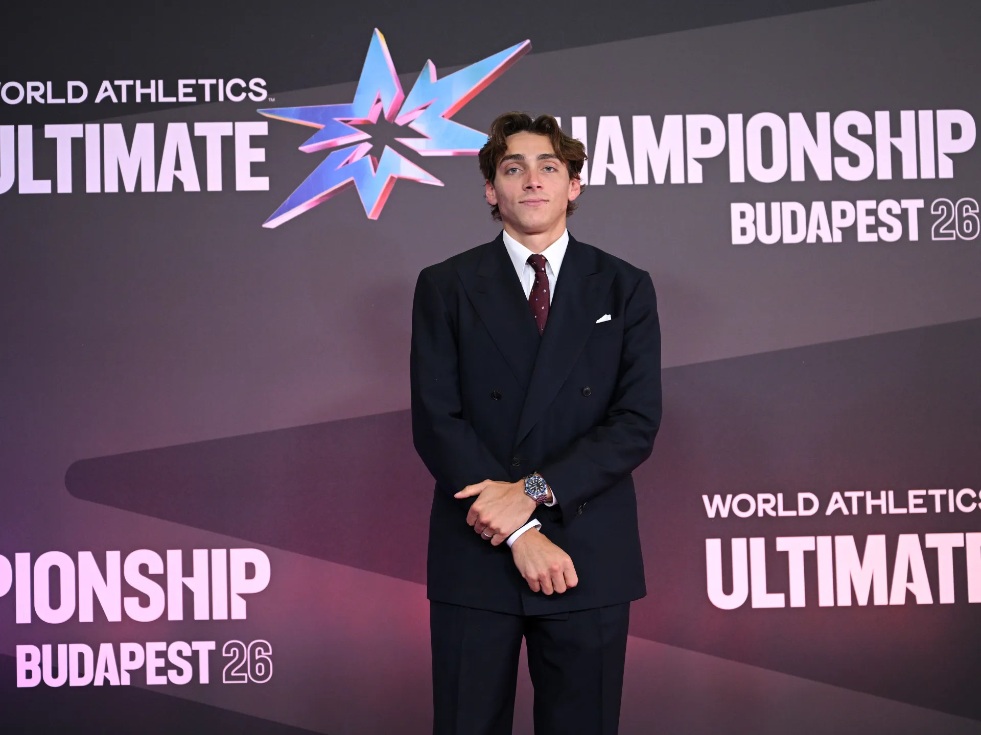 Suited athlete standing before a World Athletics Ultimate Championship Budapest 26 backdrop