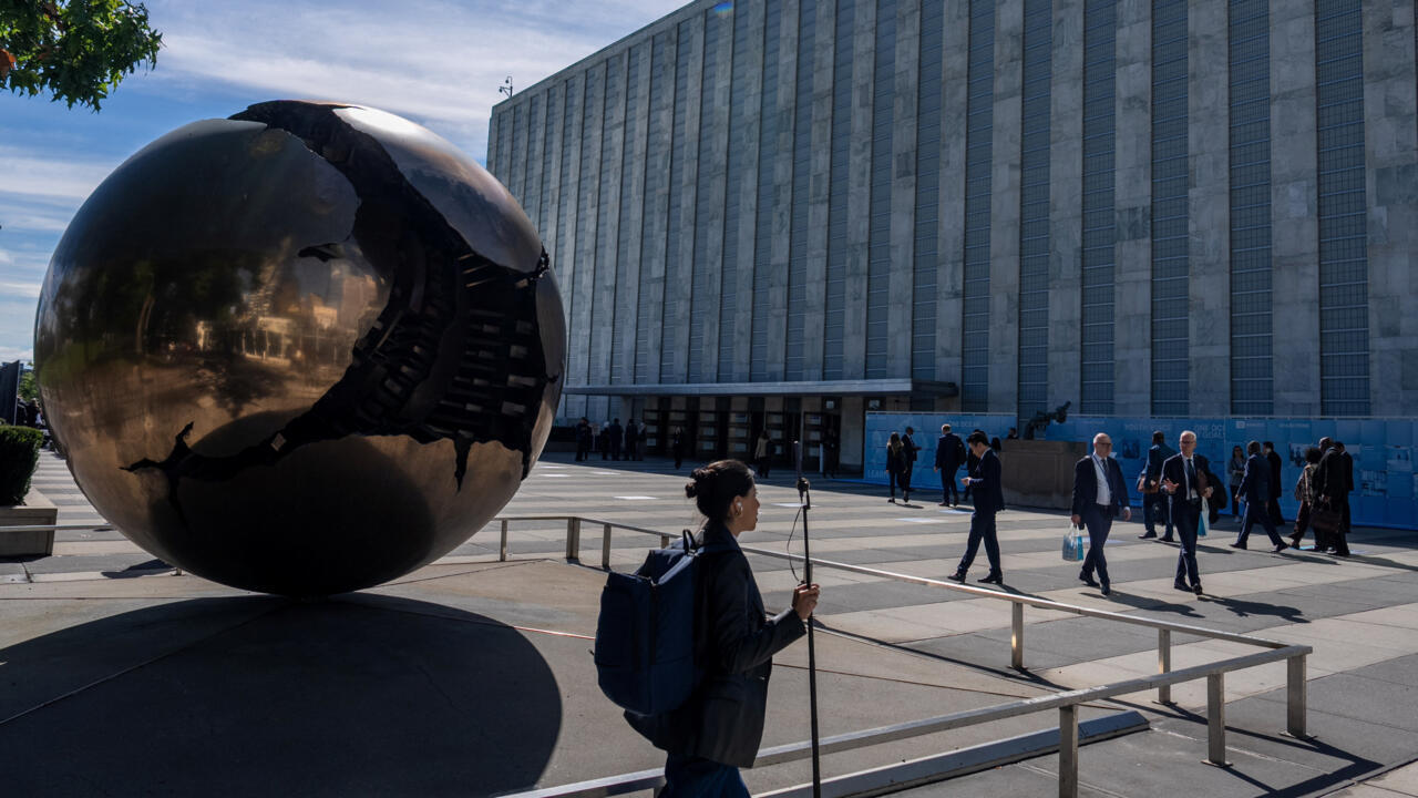 People walk past a reflective globe sculpture outside a large institutional building.