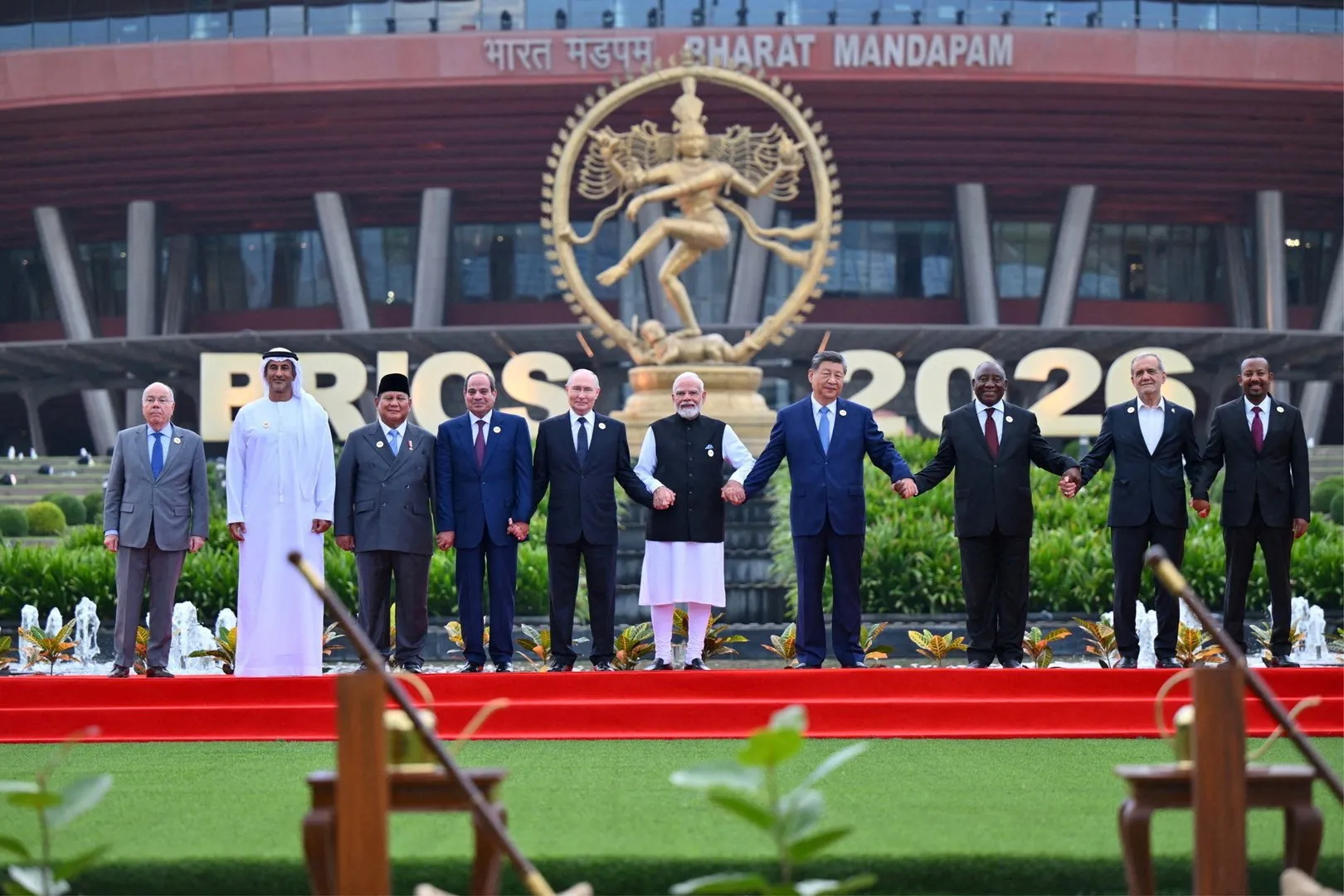 World leaders stand hand in hand before a BRICS 2026 display and Nataraja statue.